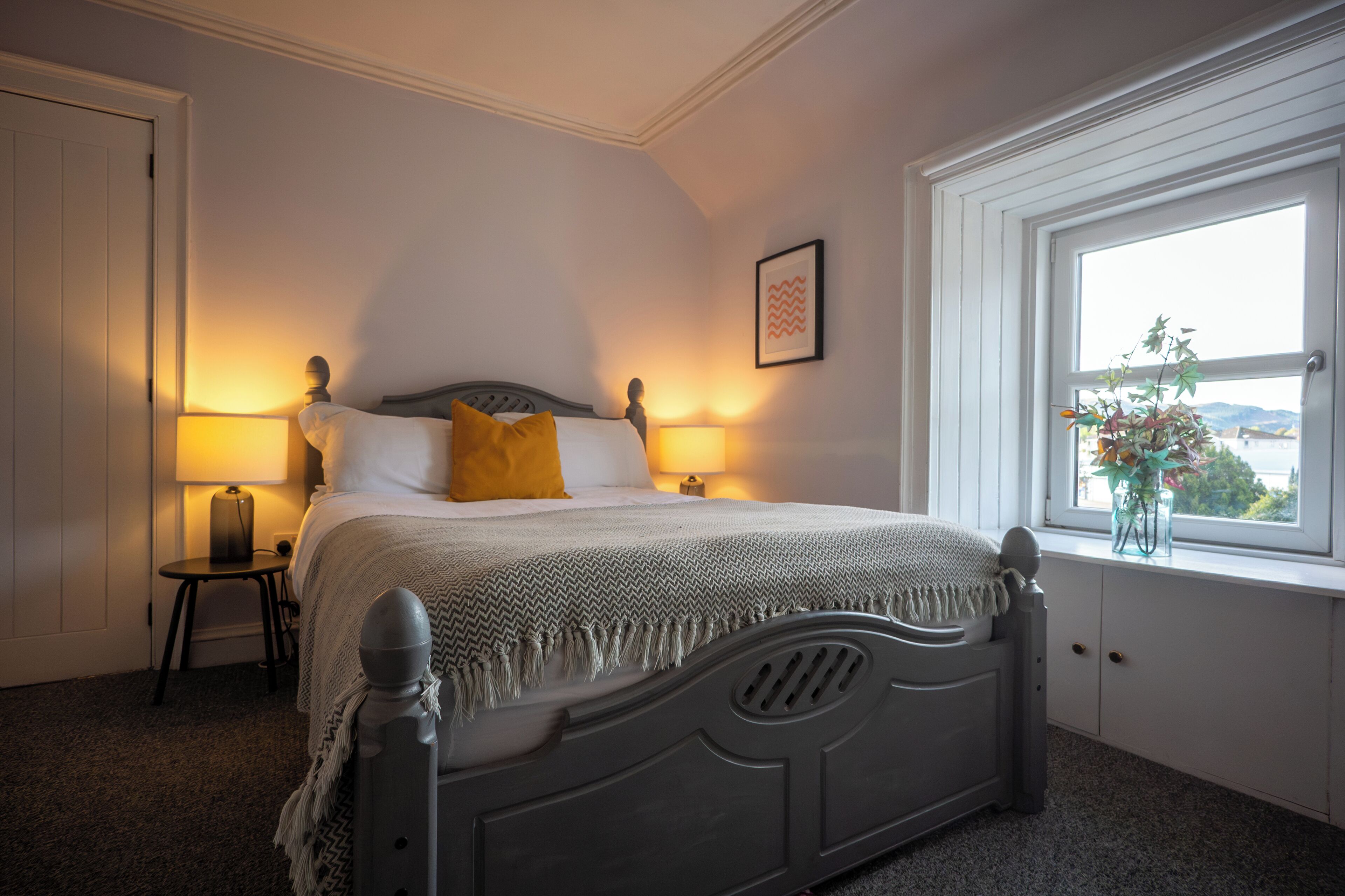 Une chambre à coucher avec un lit, des lampes de chevet, une fenêtre donnant sur un paysage agréable et une porte.