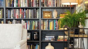 A cozy reading nook with a bookshelf filled with books, a comfortable armchair, and a small table with a lamp and decorative items. - County Seat Colonial  (Litchfield)