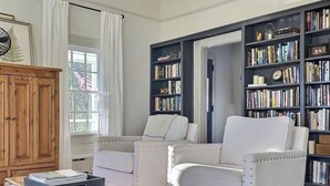 A living room with a large bookshelf, two white armchairs, a wooden chest of drawers, and a patterned rug. - County Seat Colonial  (Litchfield)