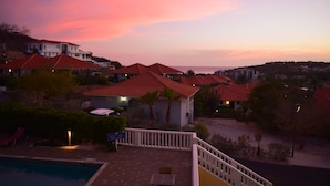Een resort met meerdere gebouwen, een zwembad en uitzicht op zee bij zonsondergang.