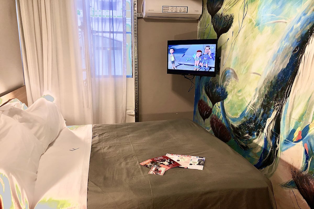 Une chambre d’hôtel avec un lit, un téléviseur fixé au mur et un tableau.