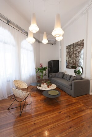 Ein modernes Wohnzimmer mit einem grauen Sofa, einem runden Couchtisch und einem Korbstuhl. Drei Pendelleuchten hängen von der Decke.