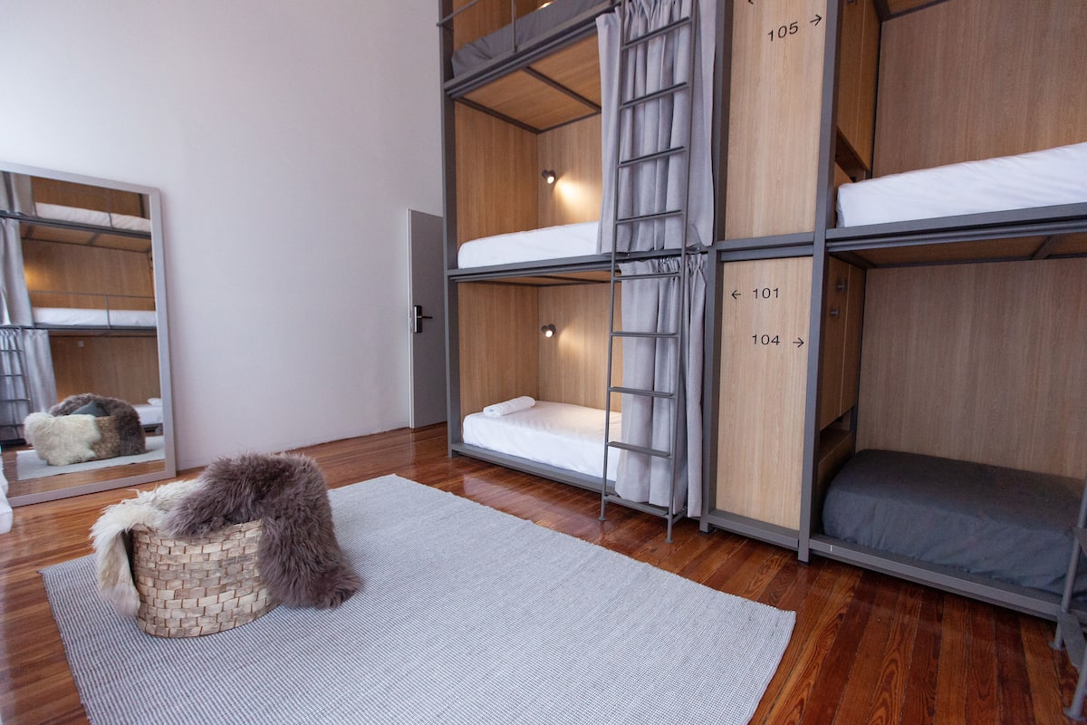 Une pièce avec des lits superposés, un plancher en bois, un panier en osier et un miroir.