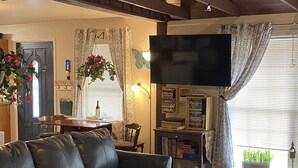 Un soggiorno con un divano in pelle nera, una TV a schermo piatto montata a parete, un tavolino in legno e una libreria piena di libri e DVD.