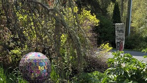 Un jardin agrémenté de fleurs violettes, une sculpture d’oiseau décorative et un globe en mosaïque.