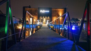 A bridge leading to a building with a 'FLO' sign, surrounded by water and illuminated lights. - Flow (Belgrade)