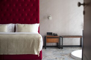 Una cama bien hecha con cabecera roja, una mesita de noche con un teléfono y un cajón pequeño.