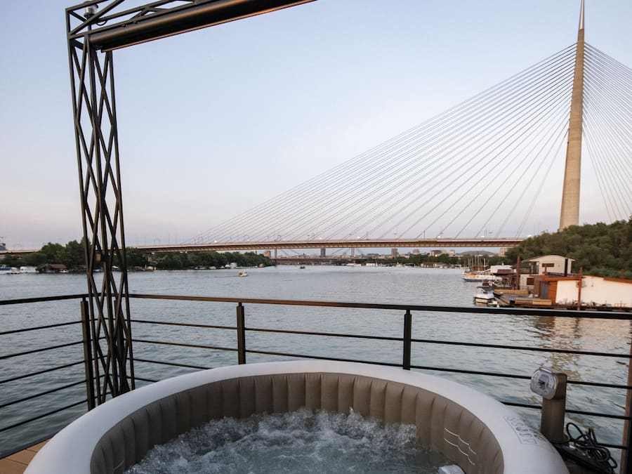 A hot tub on a deck with a view of a bridge and river.