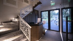 A reception area with a wooden desk, a staircase with decorative railings, and a view of an outdoor deck. - Flow (Belgrade)