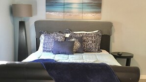 Et soveværelse med seng, loftventilator, natbord, lampe og et kunstværk på væggen.