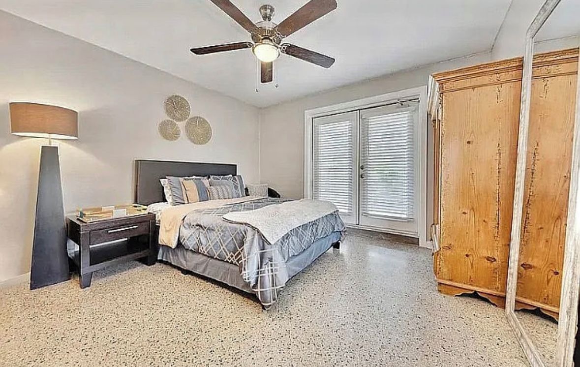 A bedroom with a bed, bedside table, lamp, ceiling fan, and a wardrobe.