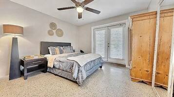 A bedroom with a bed, bedside table, lamp, ceiling fan, and a wardrobe.