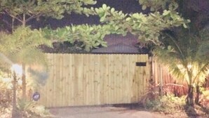 Een houten poort met een metalen grendel, omringd door begroeiing en een geplaveid pad.