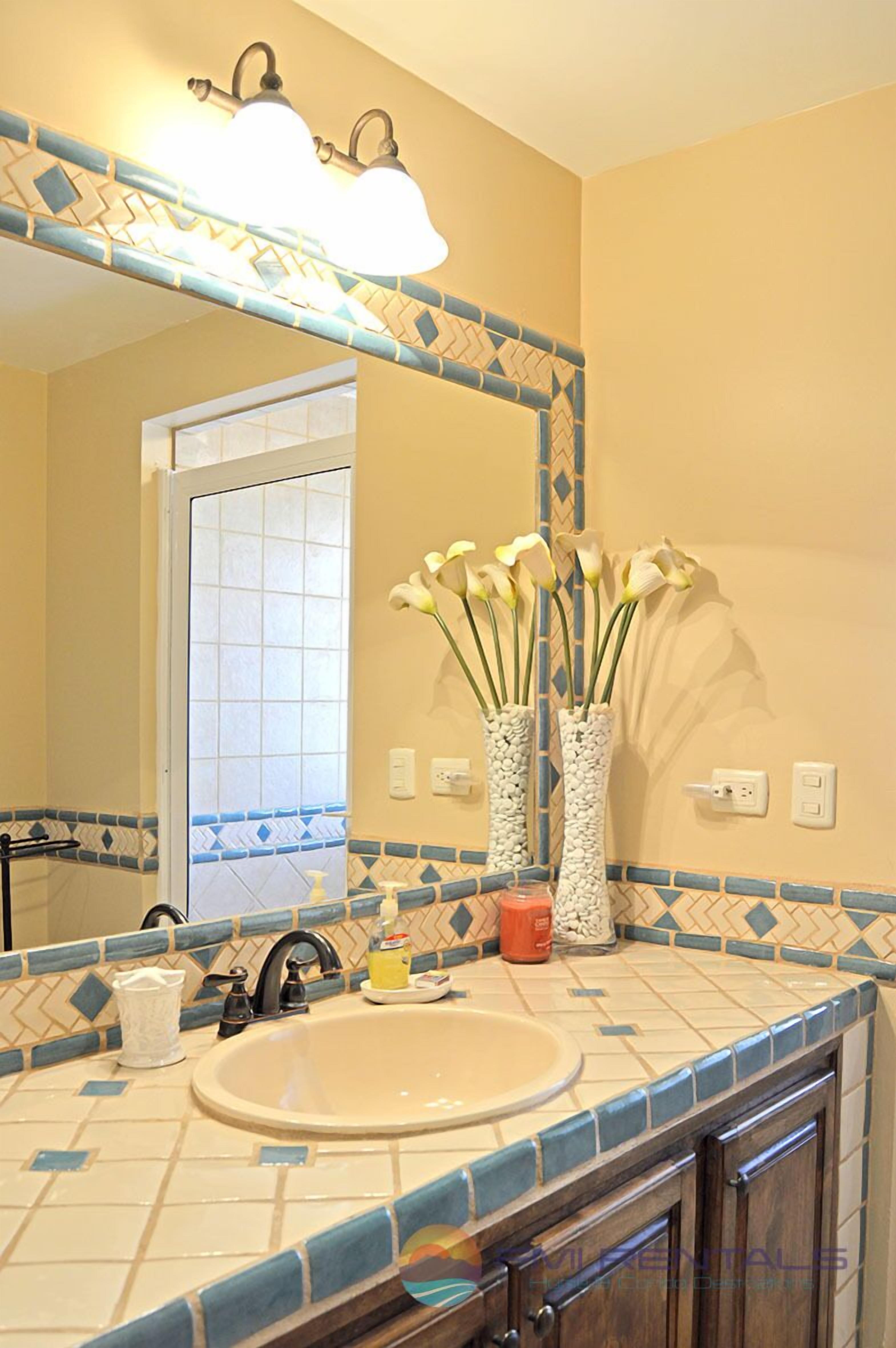 Un baño con lavamanos, espejo y jarrones decorativos.
