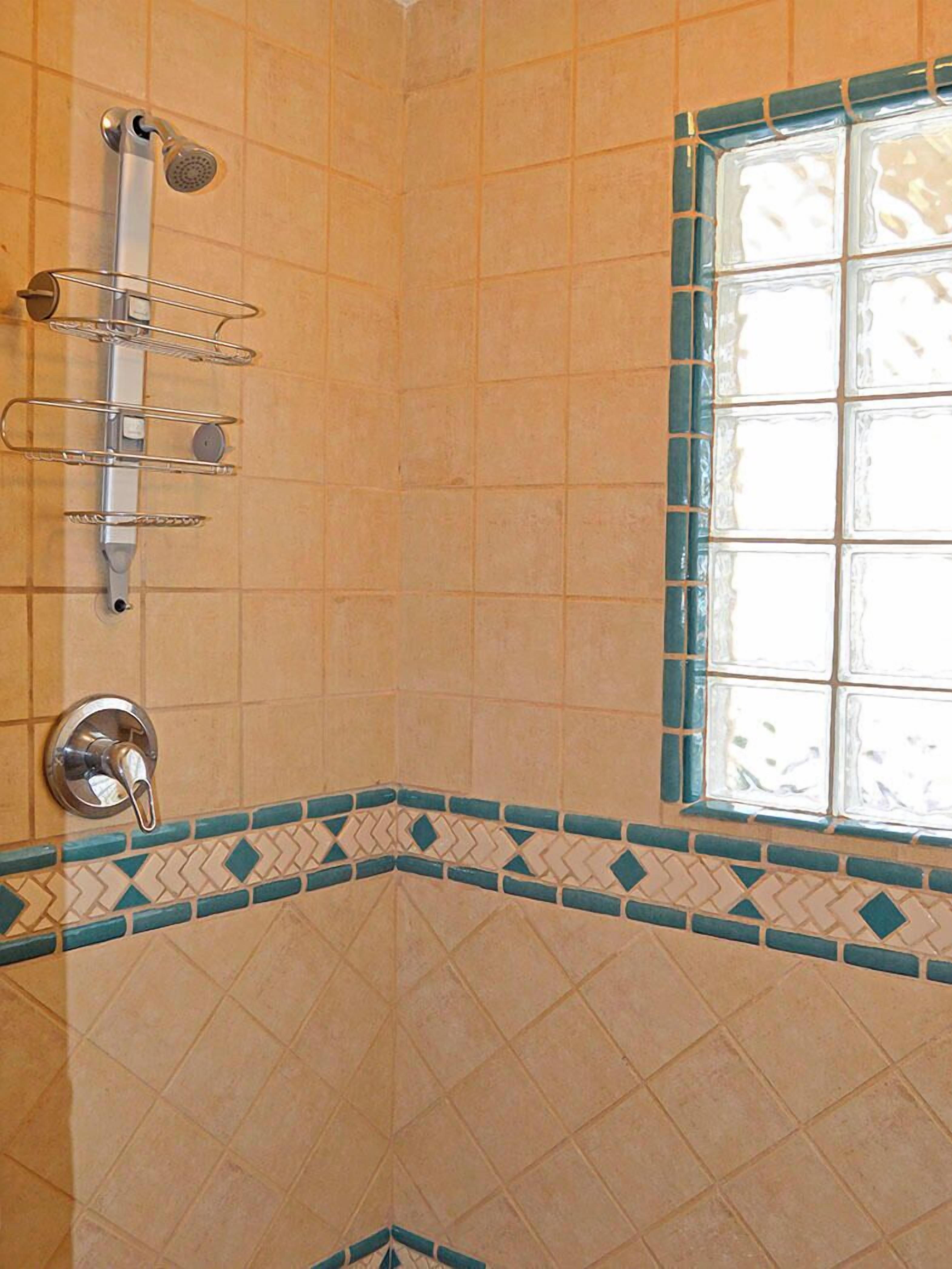Un bagno con doccia, pareti piastrellate e una finestra con vetro decorativo.