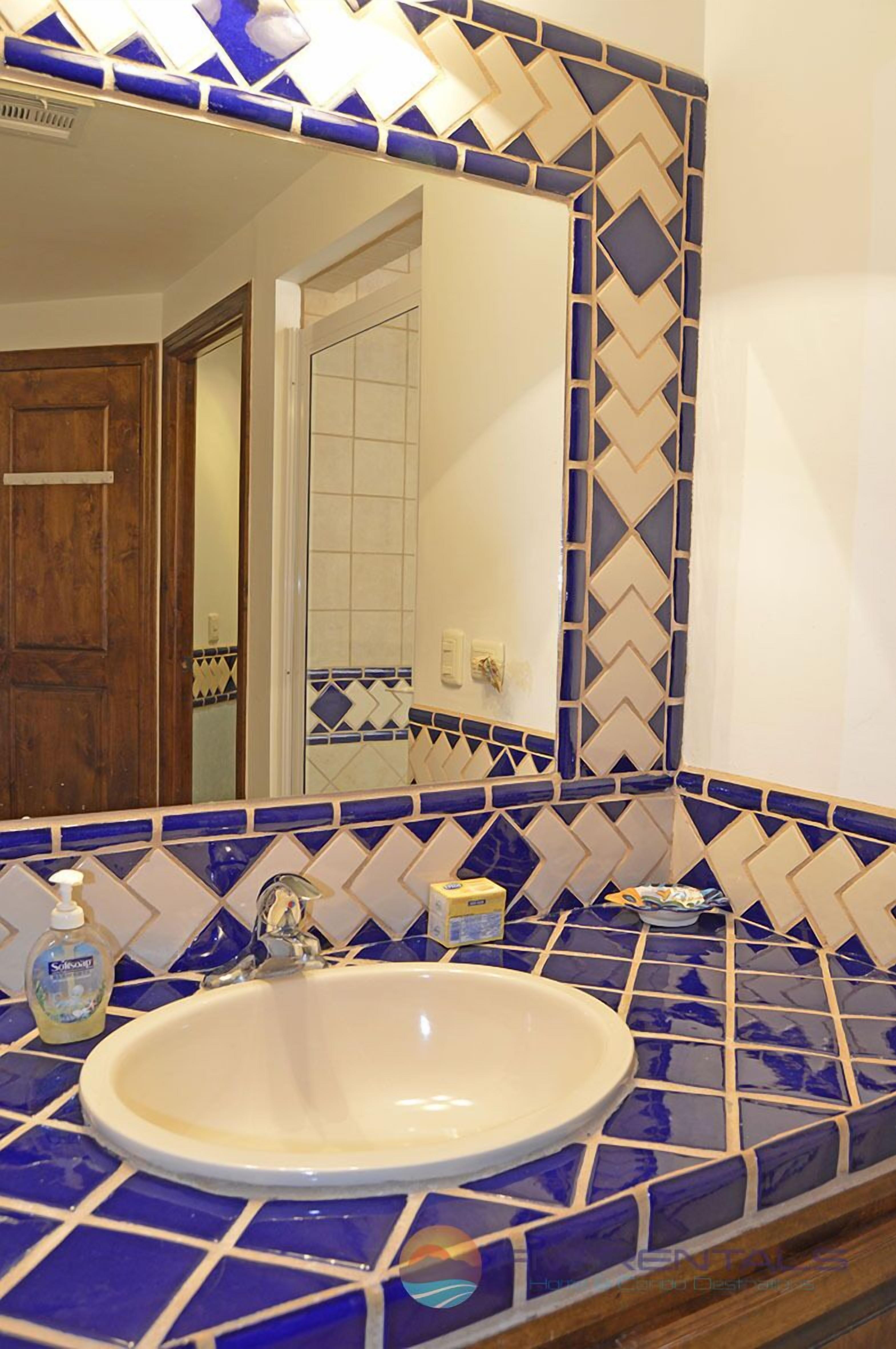A bathroom with a large mirror, a sink, and blue and white patterned tiles.