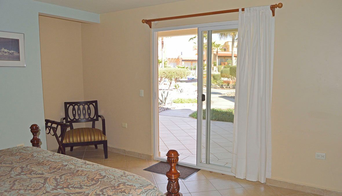 A bedroom with a bed, a chair, and a sliding glass door to a patio.