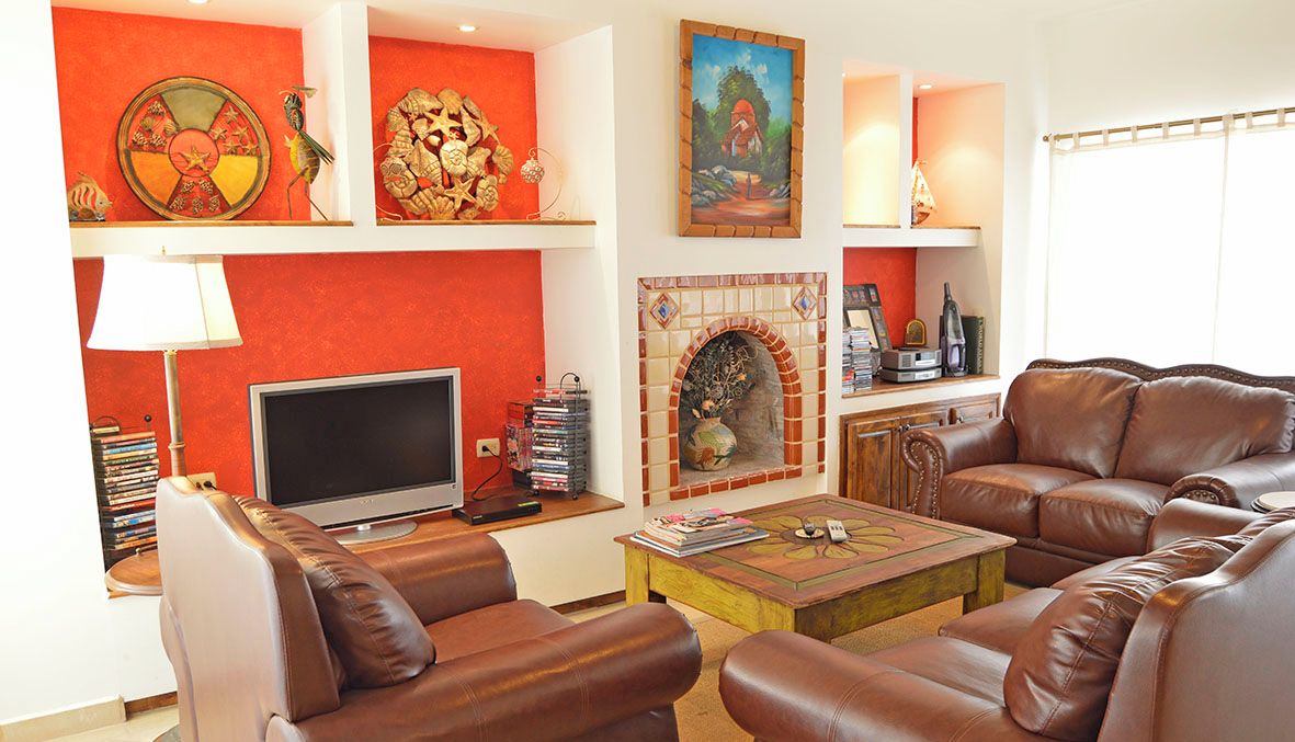 Ein Wohnzimmer mit Ledersofas, einem Flachbildfernseher, einem Kamin und verschiedenen dekorativen Objekten auf Regalen.