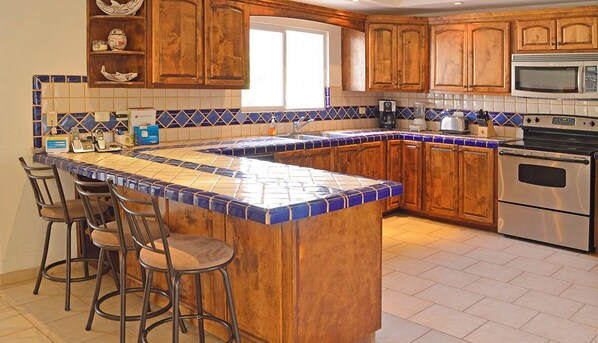 Cocina con armarios de madera, salpicadero de azulejos, una isla grande con taburetes y electrodomésticos de acero inoxidable.