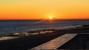 A sunset over the ocean with a beach and a tiled walkway.