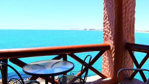 Vista al mar con una mesa y sillas, barandilla de madera y cielo azul despejado.