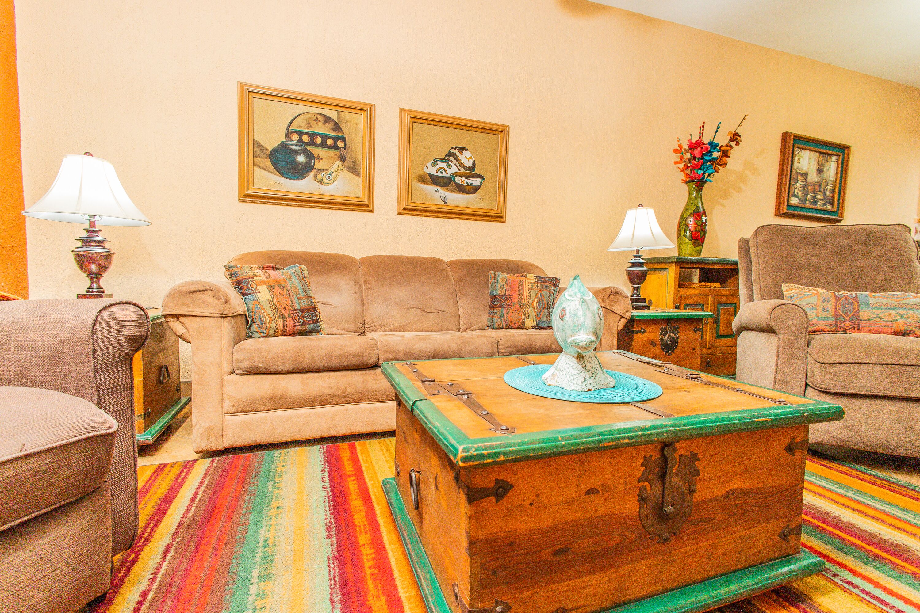 Una sala de estar con sofá, sillones, un cofre de madera y alfombras coloridas.