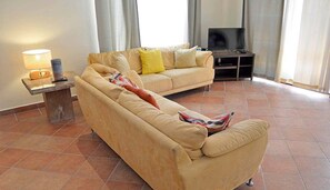 Un salon avec un canapé beige, une petite table avec une lampe et un téléviseur.