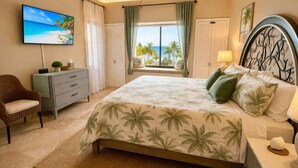 Ein Schlafzimmer mit einem Bett, einem Sessel, einem Schminktisch, einem Fernseher, einem Fenster mit Vorhängen und einem Deckenventilator.