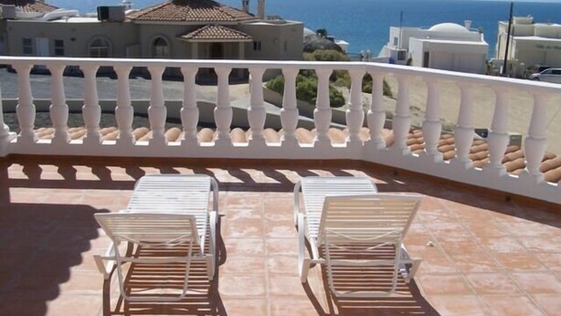 Ein Balkon mit zwei weißen Stühlen und einem weißen Geländer mit Blick auf die Küste.