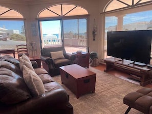 A living room with a leather sofa, a television, and a view of the sea through large windows.