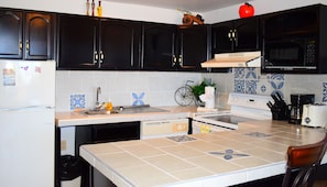 Compact kitchen with a refrigerator, stove, microwave, and sink, featuring a modern faucet and a bicycle decoration.