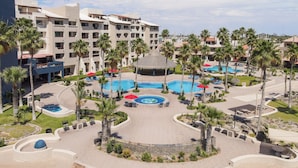 Een resort met meerdere zwembaden, palmbomen en een groot gebouw met balkons.