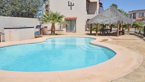 Une piscine à bord incurvé, entourée d’une terrasse en pierre. On y trouve également une structure à toit de chaume et un palmier à proximité.