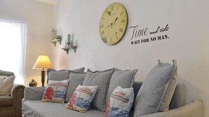 Un salon avec un canapé gris, des coussins décoratifs, une horloge murale et une citation inspirante.