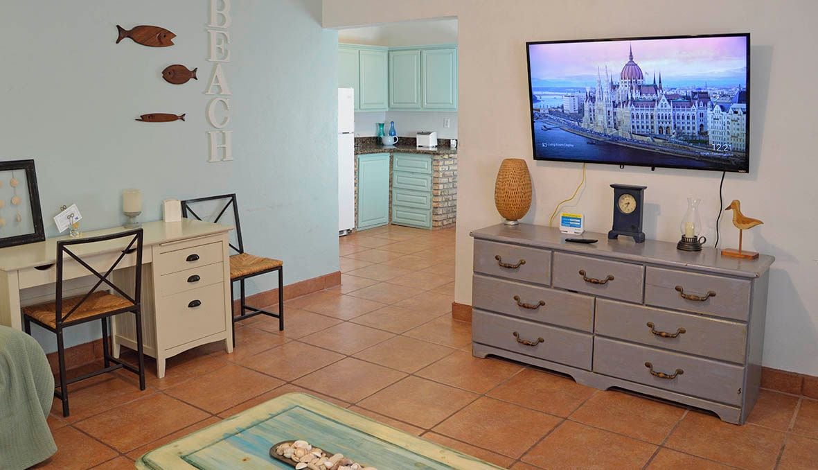 A living room with a television displaying a cityscape, a dining area with a table and chairs, and a kitchen in the background.