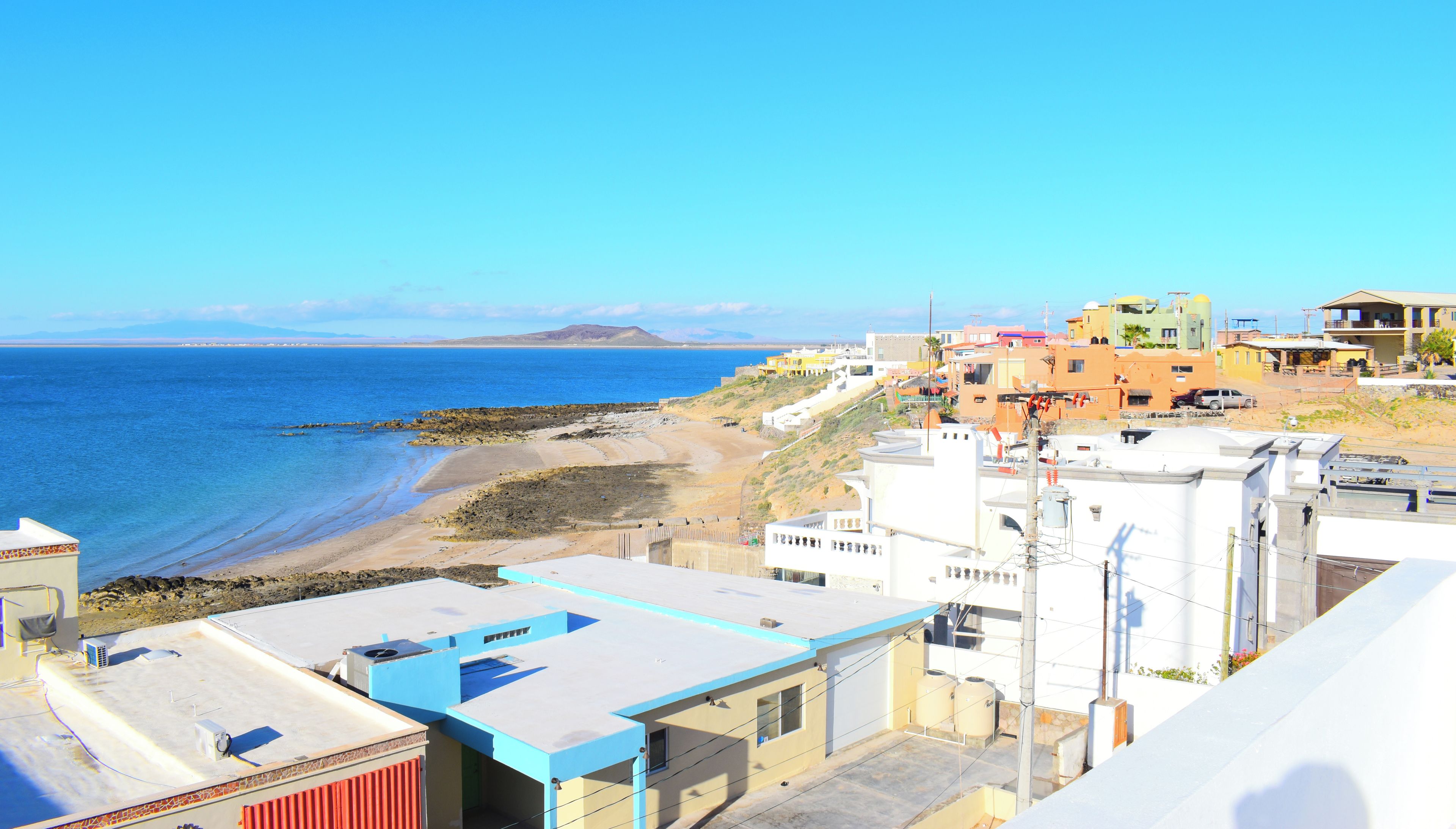 Une vue côtière avec des bâtiments, une plage et des montagnes à l’horizon.