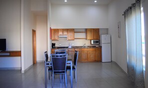 A compact kitchen with wooden cabinets, a microwave, and a refrigerator. There is a dining area with a table and chairs.