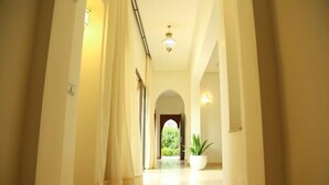 A well-lit corridor with a potted plant, a chandelier, and an archway leading to a garden. - The Villa of Peace. (Marrakech)