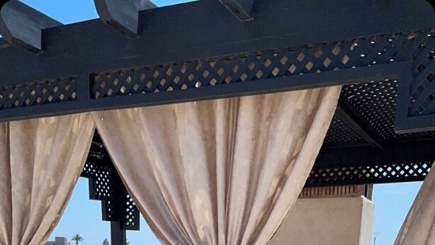 An outdoor seating area with wooden pallets, cushioned seating, and a pergola with draped fabric. - The Villa of Peace. (Marrakech)