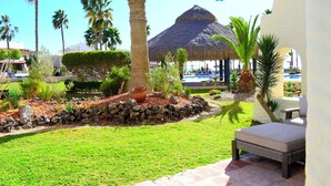 Un resort con piscina, sillas de descanso, palmeras y una estructura de techo de paja.