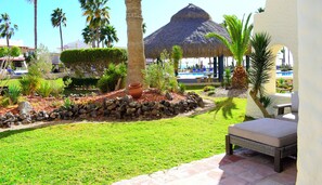 Un resort con piscina, sillas de descanso, palmeras y una estructura de techo de paja.