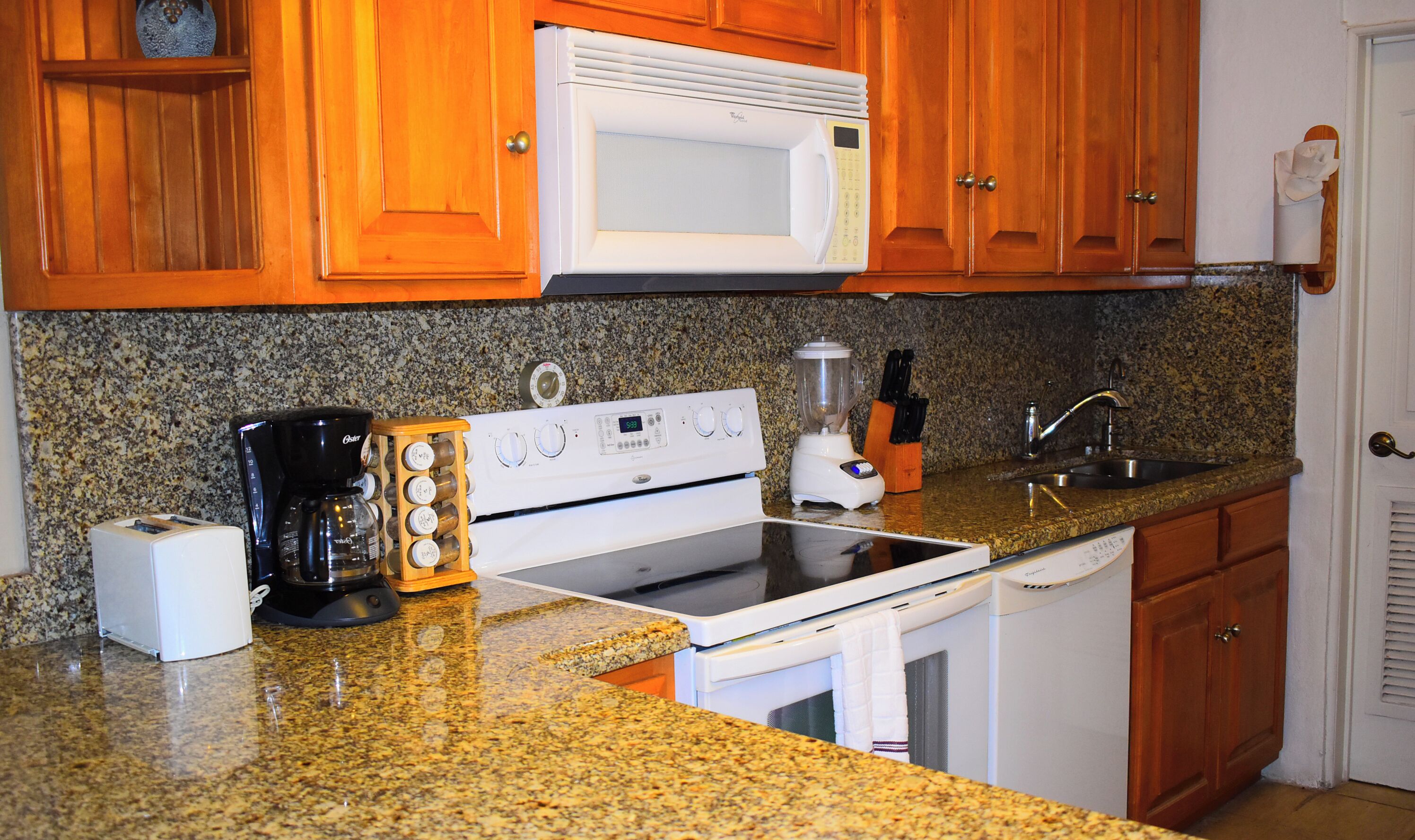 A kitchen with wooden cabinets, a white microwave, a stove, a blender, and a coffee maker.