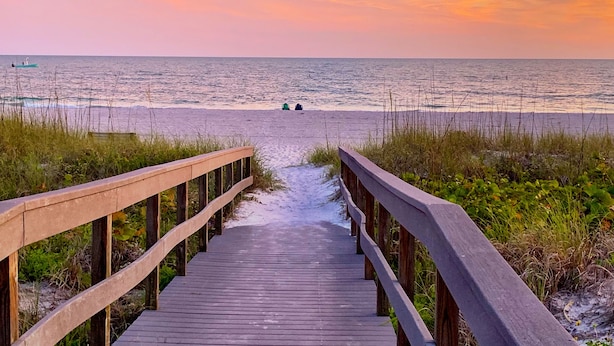 A wooden boardwalk leading to a beach with a view of the ocean and a sunset.