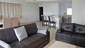 A modern living room with two dark leather sofas, a coffee table, and a dining area with a kitchen in the background.