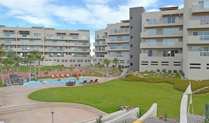 A modern hotel with multiple floors, a swimming pool, and well-maintained outdoor areas including a lawn and rock garden.