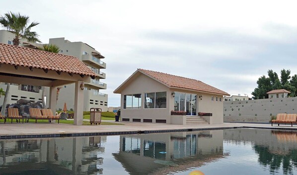 A resort with a swimming pool, lounge chairs, and a small building with a tiled roof.