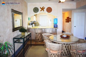 Cozy dining area with a round table and wicker chairs, featuring a side table with a potted plant and a mirror with a decorative frame.