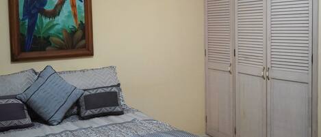A bedroom with a bed, pillows, a painting of parrots, and a wardrobe.