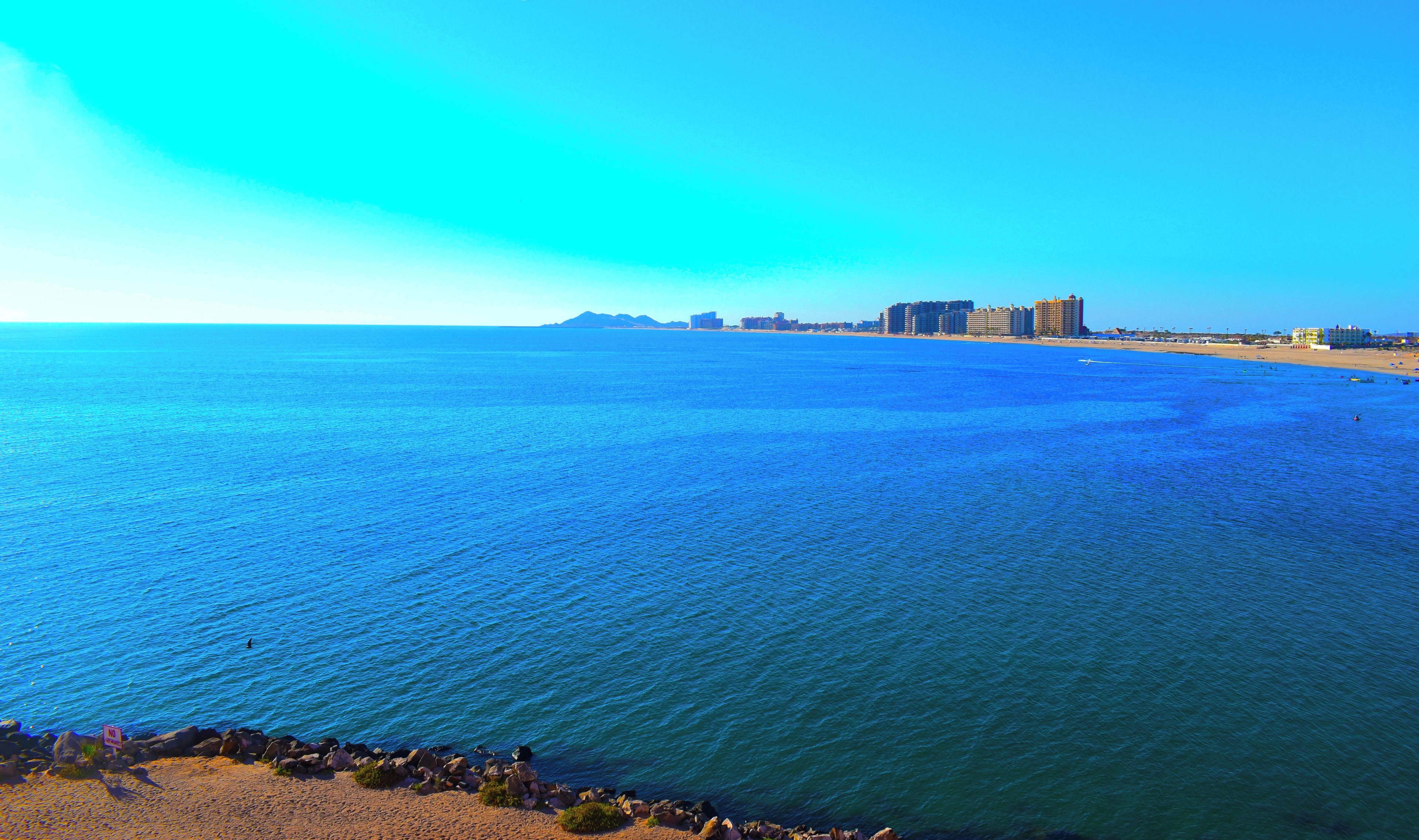 Blick auf die Küste mit blauem Himmel, Sandstrand und felsiger Küstenlinie.