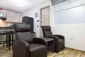Un espacio habitable compacto con dos sillones reclinables, una pequeña zona de cocina y un reloj en la pared.